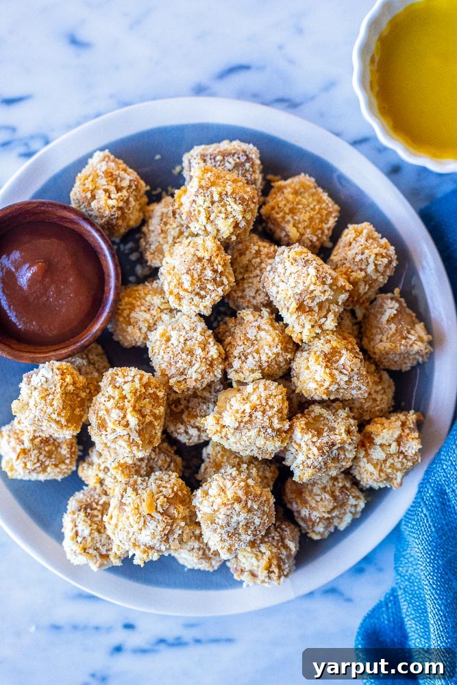 Crispy Tofu Poppers 2 A vibrant plate full of golden-brown crispy tofu nuggets, accompanied by small bowls of bright red ketchup and creamy honey mustard dipping sauces.