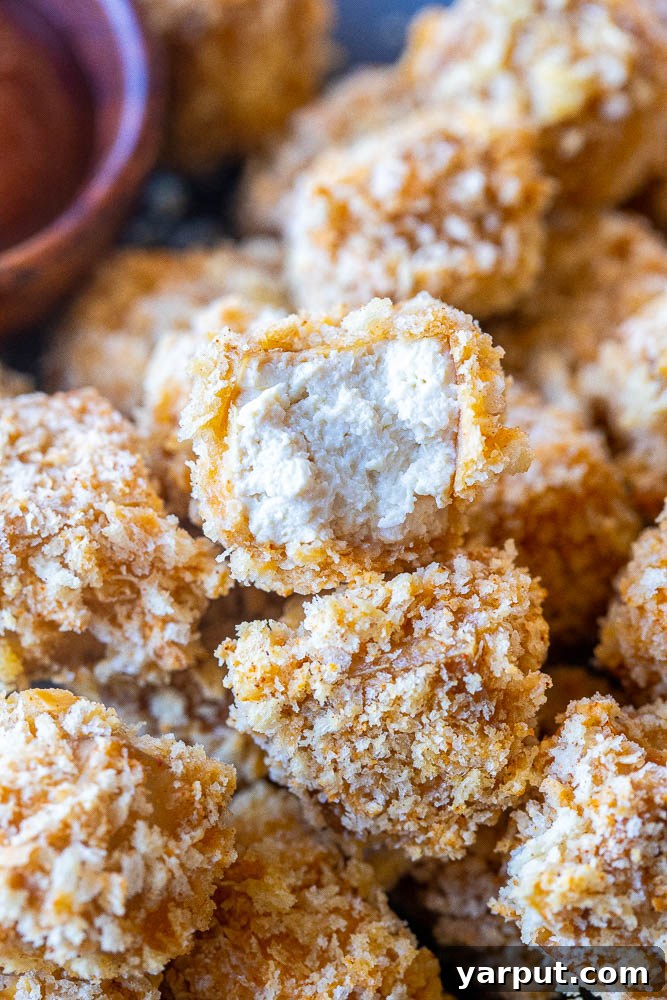 Crispy Tofu Poppers 4 A close-up shot of a golden-brown crispy tofu nugget with a bite taken out, revealing its tender, flavorful interior texture.