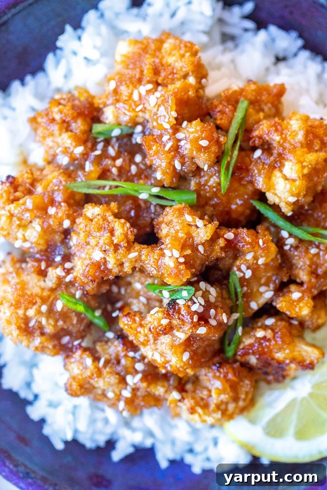 Lemon-Glazed Roasted Cauliflower 5 A close-up shot of a full bowl of sticky lemon cauliflower, garnished with sesame seeds and green onions, ready to be served. The rich sauce and crispy texture are clearly visible.