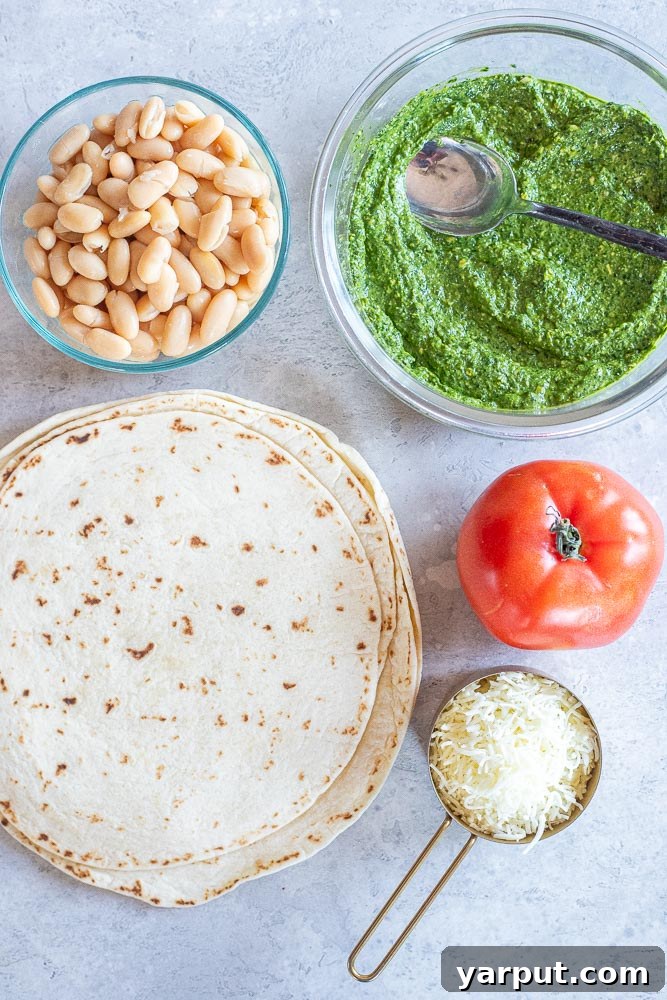 Creamy White Bean Pesto Quesadillas with Fresh Tomato 3 Showing the fresh ingredients for making pesto quesadillas with white beans and tomato: tortillas, pesto, cheese, tomatoes, and canned white beans