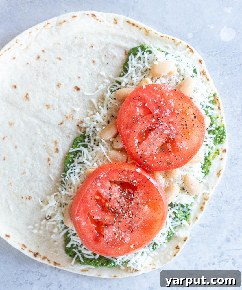 Creamy White Bean Pesto Quesadillas with Fresh Tomato 4 Step-by-step image showing how to assemble pesto quesadillas: a tortilla with pesto, cheese, white beans, and tomato on one half