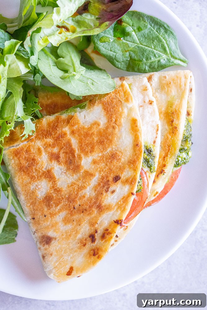 Creamy White Bean Pesto Quesadillas with Fresh Tomato 5 Overhead shot of two pesto quesadillas sliced and served on a plate with a fresh green salad
