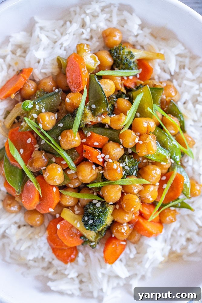 Close-up of a generous serving of honey garlic chickpeas and vegetables over rice in a white bowl, ready for a healthy meal.