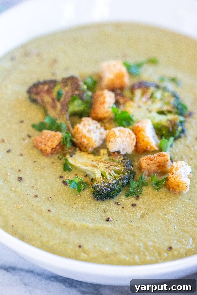 Close-up of a rustic bowl of roasted broccoli soup, beautifully garnished with crunchy croutons and a fresh herb sprig.