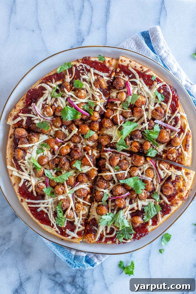 Smoky BBQ Chickpea Pizza 4 A slice of BBQ Chickpea pizza resting on a white plate, showcasing the rich toppings and golden crust