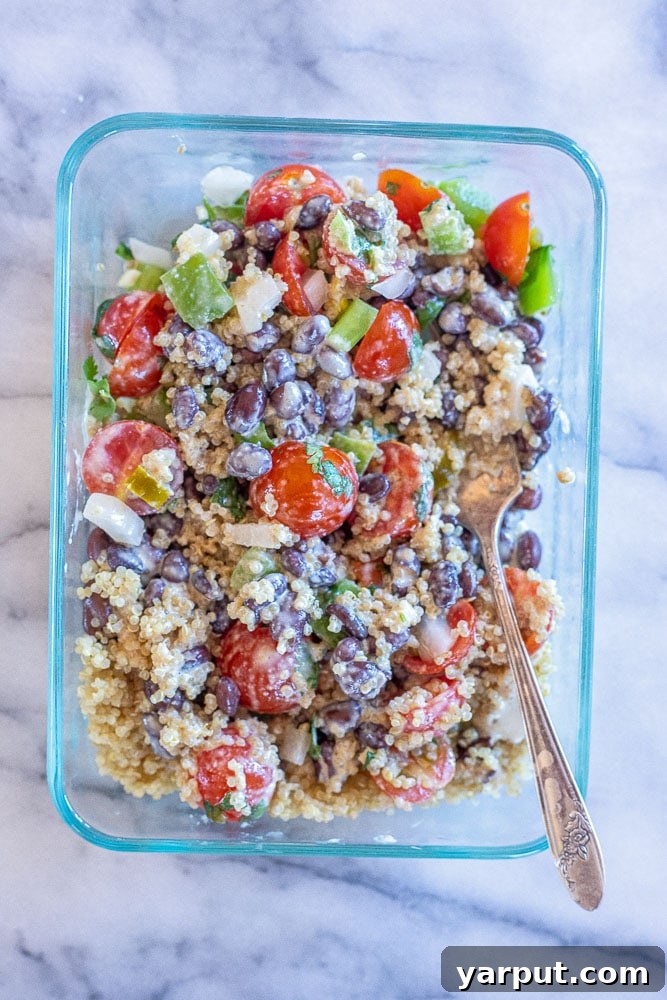 A close-up shot of a Mexican quinoa salad bowl, with all ingredients mixed together, showing fluffy quinoa, black beans, vibrant tomato salsa, and a creamy dressing, ready to eat