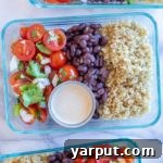 A top-down view of a vibrant Mexican Quinoa Salad Bowl, featuring quinoa, black beans, corn, red bell pepper, and cilantro, with a creamy dressing drizzled over it, presented in a white bowl.