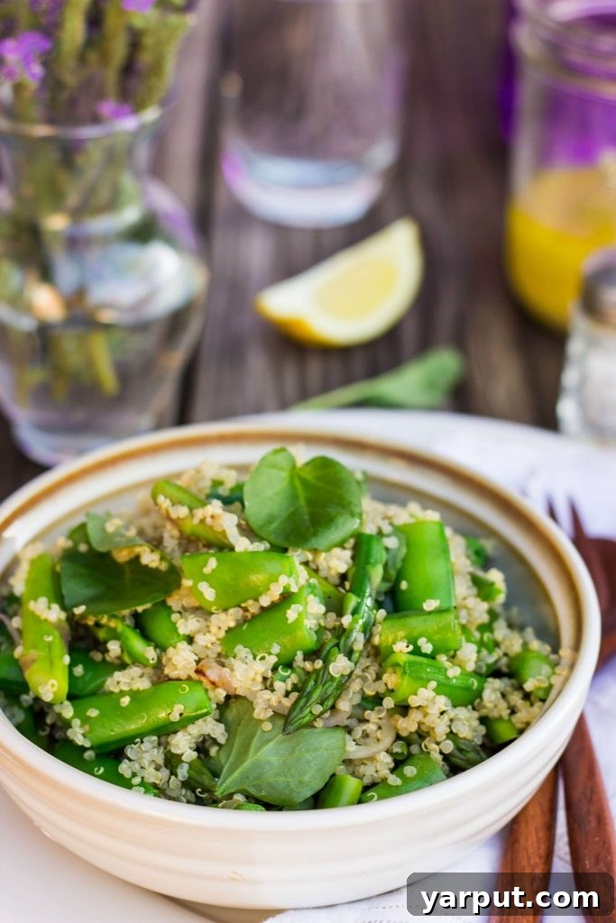 A beautifully presented Spring Quinoa Salad in a large white bowl, garnished with fresh herbs and a wooden fork, showcasing the vibrant green of asparagus and sugar snap peas mixed with fluffy quinoa and watercress.