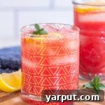 A glass of vibrant watermelon lemonade with a lemon slice and mint garnish.