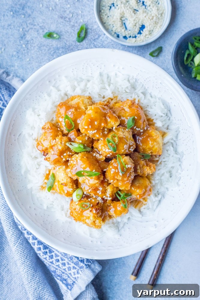 Crispy Zesty Vegan Orange Chicken 5 A beautifully presented bowl of vegan orange chicken, served over fluffy white rice and garnished with fresh green onions and sesame seeds, ready for a delicious meal.
