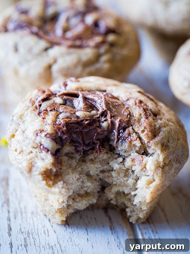 Nutella Marbled Banana Muffins 6 A delectable banana muffin with a Nutella swirl, showing a bite taken out, revealing its moist texture and rich filling.