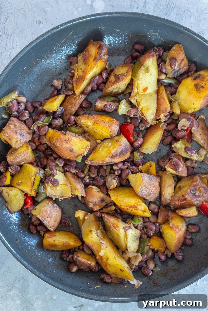 Trader Joe's Five Series: Spicy Potato Tacos with Black Beans 4 Close-up view of cooked roasted potatoes with peppers and onions mixed with seasoned black beans in a pan, ready to be scooped into tacos.