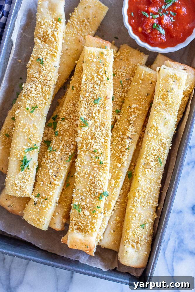 Irresistible Vegan Breadsticks 2 Deliciously golden-brown vegan breadsticks served on a baking pan with a side of marinara dipping sauce.