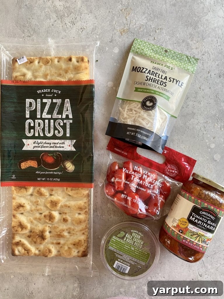 Trader Joe's Simple 5-Ingredient Vegan Tomato Pesto Pizza 3 Ingredients laid out for making vegan pesto pizza, including pizza crust, marinara, vegan pesto, dairy-free cheese, and mini plum tomatoes
