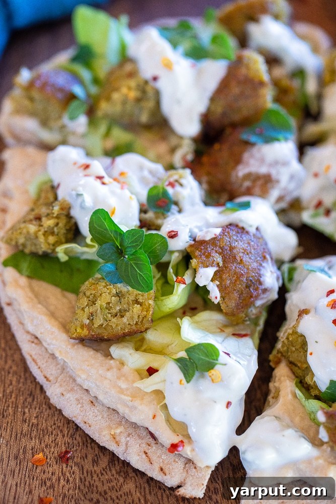 Loaded Vegan Falafel Pitas 5 Close-up photo of a fully assembled open-faced vegan falafel pita, showing layers of hummus, lettuce, falafel, and tzatziki sauce