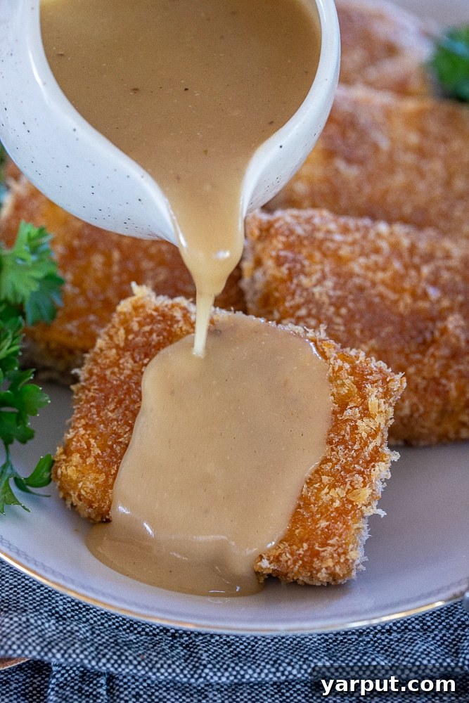 Golden Crispy Tofu Steaks 5 Rich vegan gravy being generously poured over a golden-brown crispy tofu steak, highlighting a delicious serving suggestion.