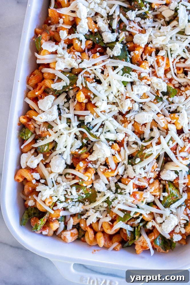 Creamy Spinach Feta Pasta Bake 4 A baking dish filled with spinach, feta, and pasta, topped with an extra sprinkle of mozzarella and feta, ready to go into the oven for baking.