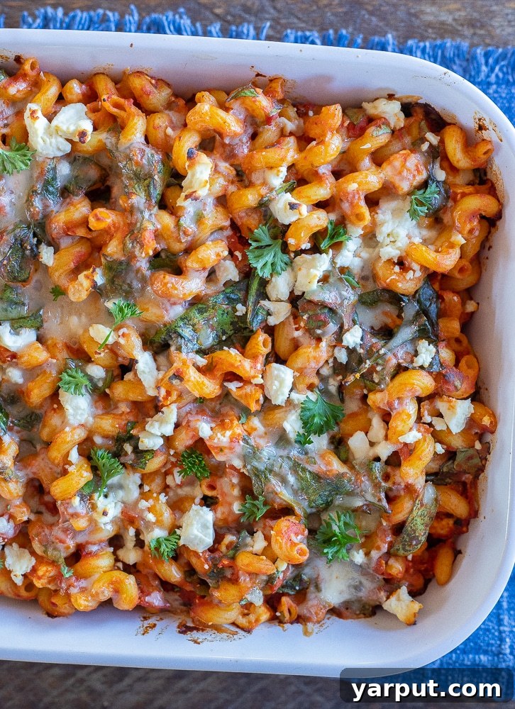 Creamy Spinach Feta Pasta Bake 6 A serving of spinach feta baked pasta in a white dish, resting on a blue linen napkin, garnished with fresh herbs, showcasing its appetizing appeal.