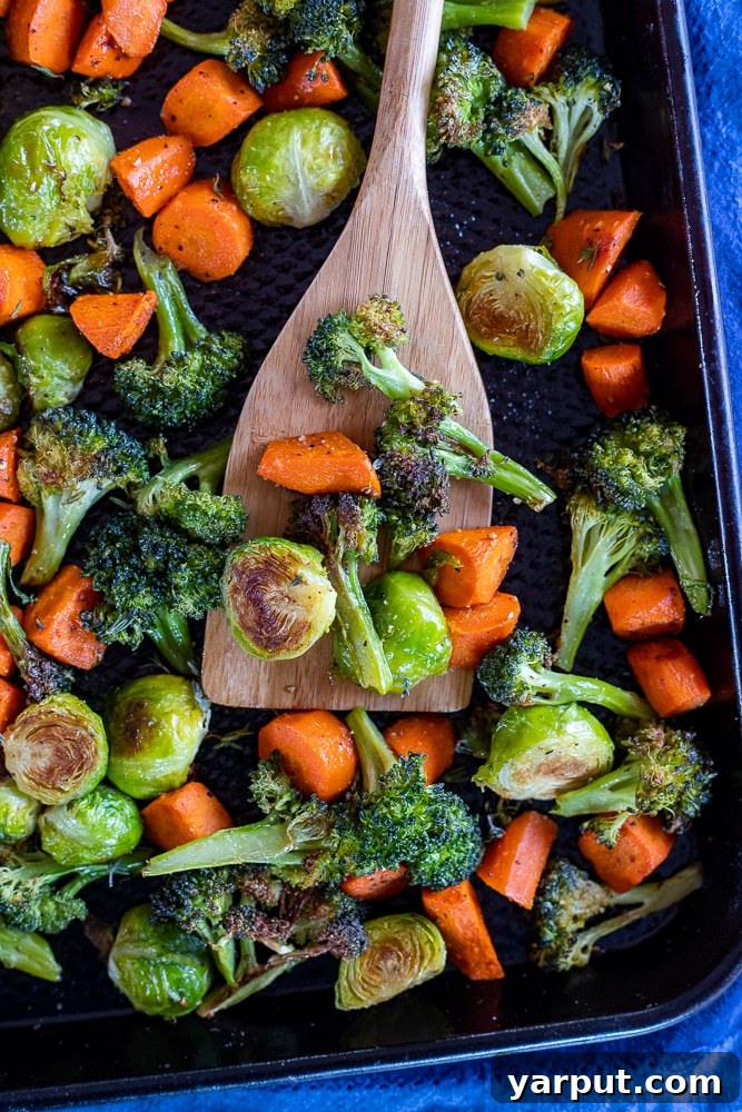 Effortless Roasted Vegetables 4 A close-up shot of perfectly golden-brown roasted vegetables, including carrots and broccoli, on a metal sheet pan, being gently lifted with a spatula, highlighting their crispy texture.