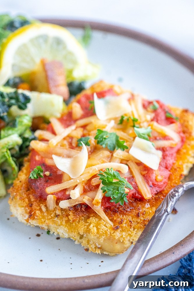 Cheesy Vegan Tofu Parmesan 5 A close-up shot of a perfectly crispy piece of Vegan Tofu Parmesan, topped with marinara and melted cheese, resting on a plate ready to be enjoyed.