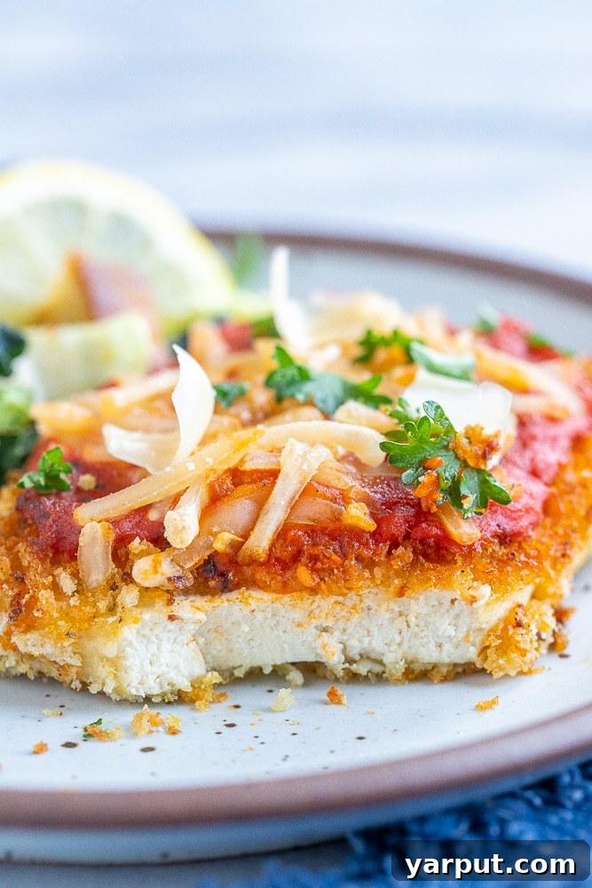 Cheesy Vegan Tofu Parmesan 6 A slice of crispy Vegan Tofu Parmesan with a bite taken out, showing the tender tofu interior and rich sauce.