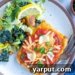 A perfectly cooked piece of Vegan Tofu Parmesan, crispy and golden brown, topped with rich marinara sauce and melted vegan cheese, served on a white plate with a side of fresh salad.