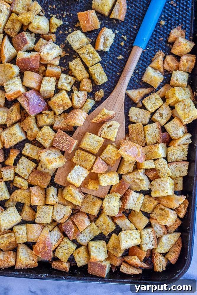 Golden Garlic Herb Croutons 5 A freshly baked tray of crispy homemade croutons, glistening with oil and seasonings, alongside a spatula.