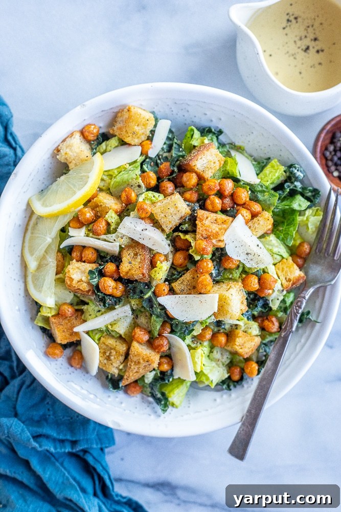 A vibrant bowl of Vegan Caesar Salad, featuring fresh romaine and kale, drizzled with creamy tahini Caesar dressing, garnished with golden croutons and crispy chickpeas, set against a serene blue napkin.