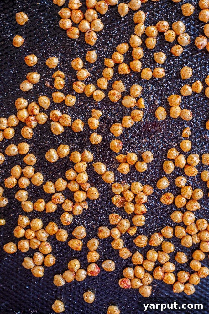 Seasoned chickpeas spread evenly on a baking sheet, golden brown and crisp, ready to be added to a delicious salad.