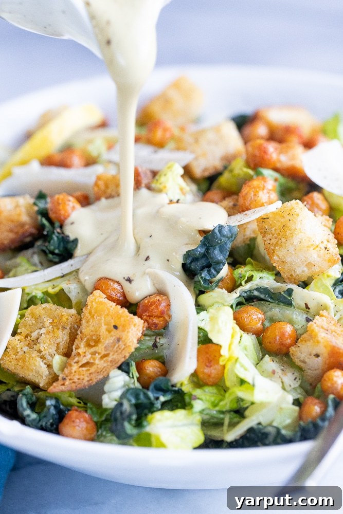 Velvety Vegan Tahini Caesar Dressing 6 vegan caesar dressing being poured on a Caesar salad, showcasing its perfect consistency