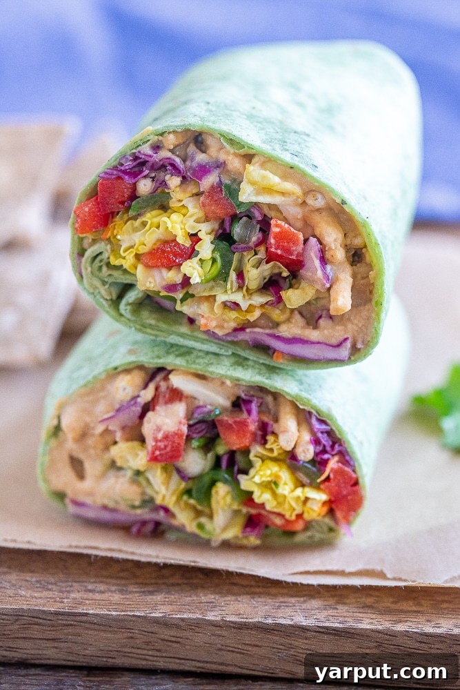 Plant-Powered Peanut Hummus Wraps 2 Two halves of a delicious peanut butter hummus veggie wrap with tofu, stacked on a plate, showcasing colorful vegetables and creamy hummus.