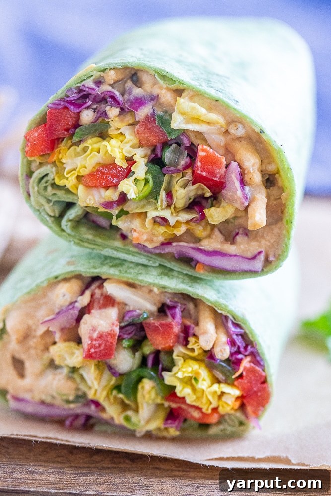 Plant-Powered Peanut Hummus Wraps 5 A close-up view of a peanut butter hummus veggie wrap with tofu, cut in half and stacked, revealing the rich layers of hummus, tofu, and colorful, seasoned vegetables, along with crunchy noodles.