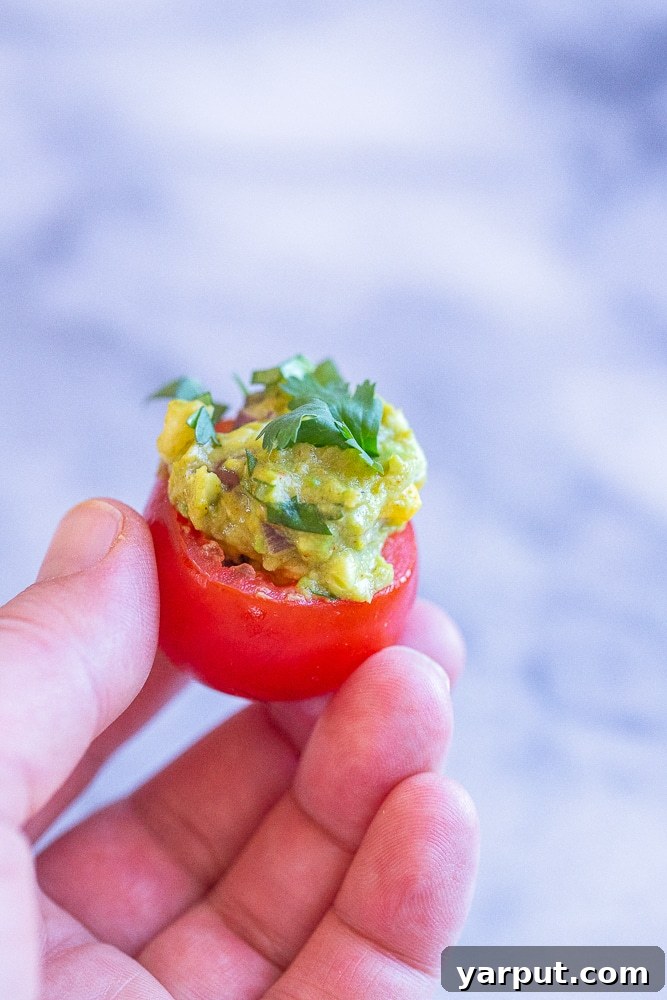 Zesty Guacamole Tomato Bites 6 A hand reaching for a perfectly prepared guacamole stuffed tomato, highlighting its appeal as a delicious, handheld snack.