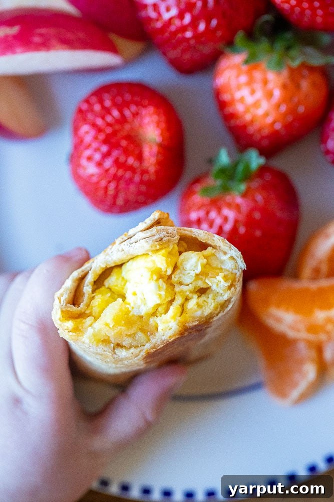 Child's hand holding a potato, egg, and cheese breakfast burrito with a bite taken out, showing the delicious filling inside.