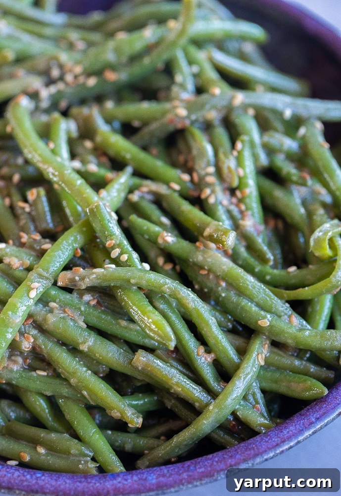 A close-up view of a purple bowl filled with the best Miso Sesame Green Beans, ready to be served, garnished with sesame seeds.