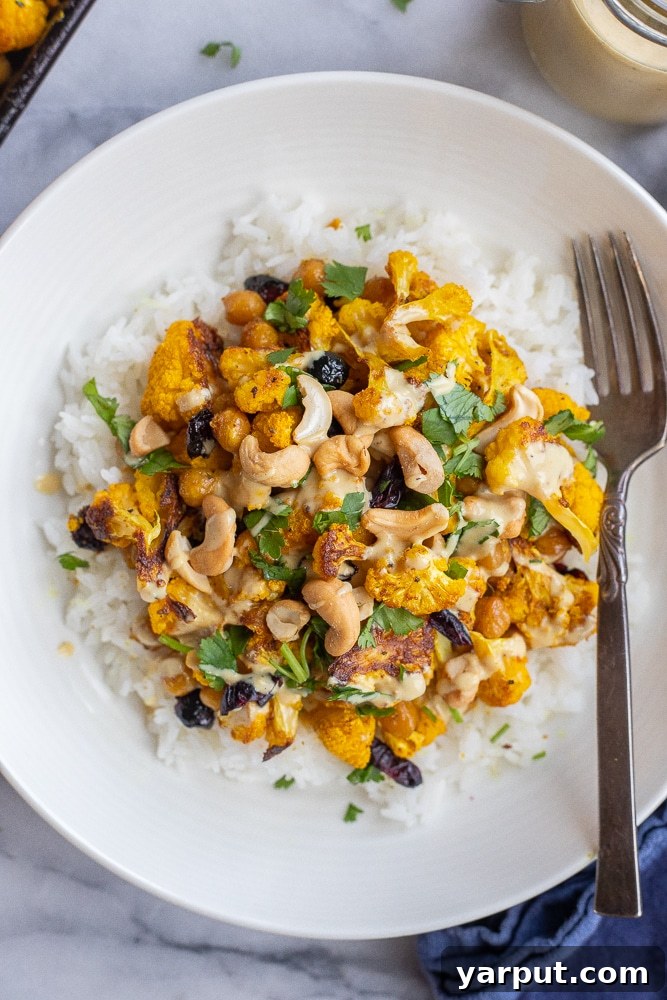 Large bowl of golden roasted cauliflower generously drizzled with coconut curry tahini dressing, garnished with fresh cilantro and cashews.