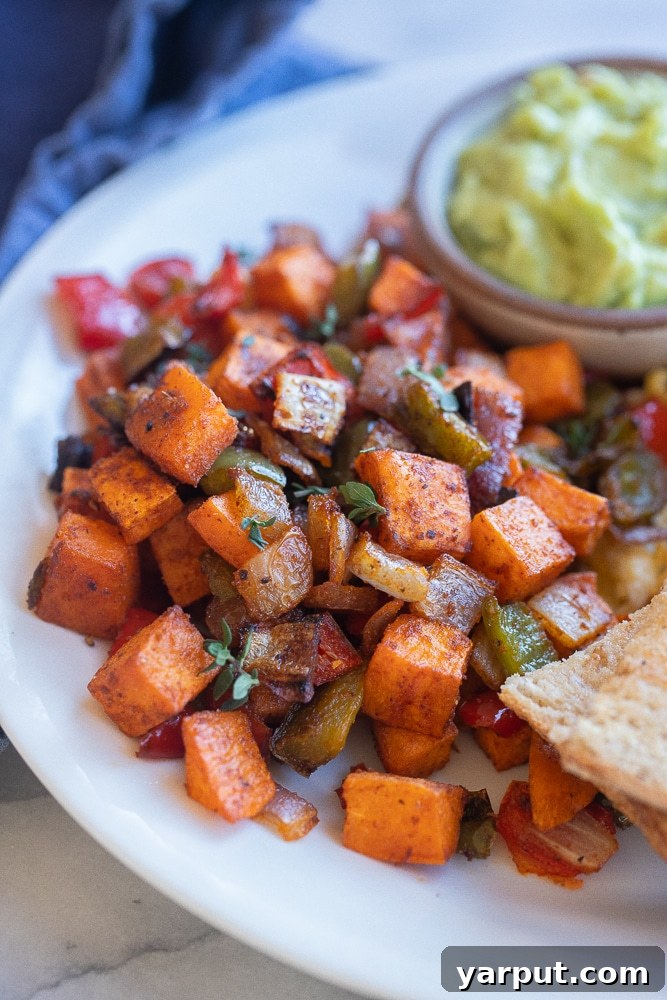 Golden Sweet Potato Skillet 2 Close up of a serving of roasted sweet potato hash on a white plate, with a fork ready to dig in. The hash features caramelized sweet potatoes, vibrant bell peppers, and onions, all seasoned to perfection, showcasing its appealing texture and rich colors.