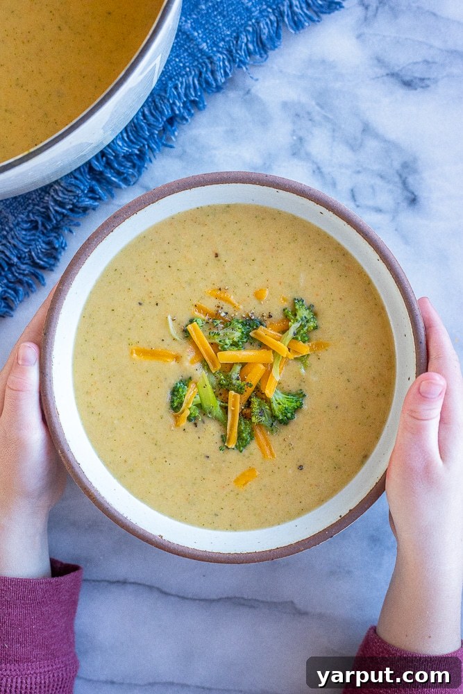 Velvety Broccoli Cheddar Soup with Fresh Vegetables 6 hands holding a bowl of creamy broccoli cheddar soup