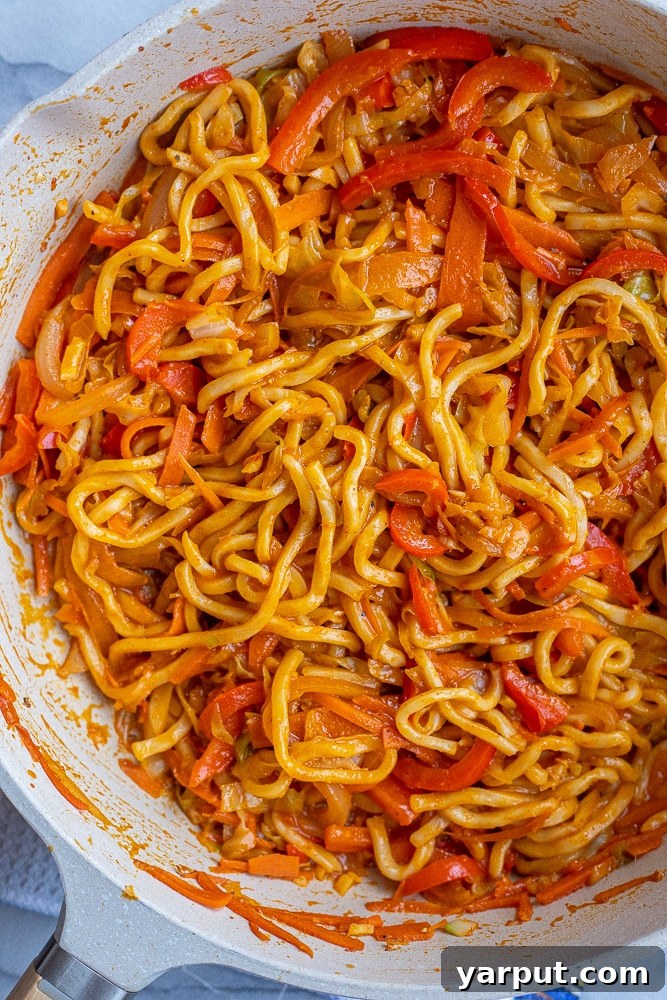 Close-up view of Red Thai Curry Noodles simmering in a large pan, coated in a rich, creamy, and vibrant sauce, with hints of mixed vegetables visible.