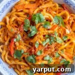 A vibrant bowl of Coconut Red Thai Curry Noodles with colorful vegetables and fresh cilantro garnish.