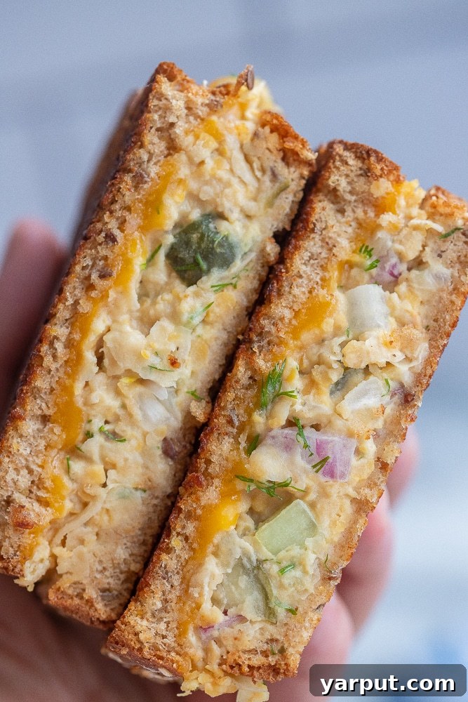 A hand holds two halves of a chickpea salad melt, showing the warm, gooey filling and toasted bread, ready to be eaten.