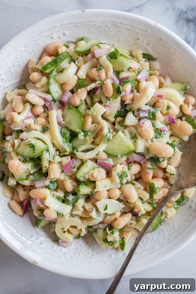 big bowl of lemony hearts of palm and white bean salad with a spoon, garnished with fresh parsley