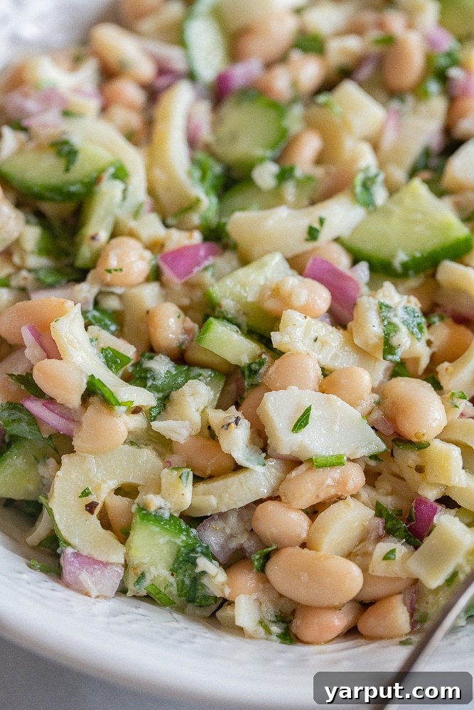 close up of a bowl of Lemony Hearts of Palm and White Bean Salad, garnished with fresh herbs