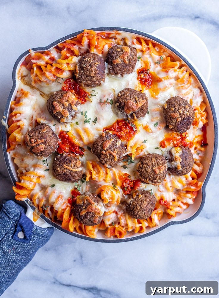Affordable Plant-Based Feasts Week 13 3 A close-up shot of spicy baked pasta with vegetarian meatballs, bubbling in a baking dish, garnished with fresh herbs, ready to be served.