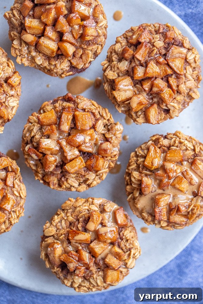 A plate of two freshly baked Caramelized Apple and Peanut Butter Baked Oatmeal Cups, topped with extra caramelized apples and a drizzle of sauce.