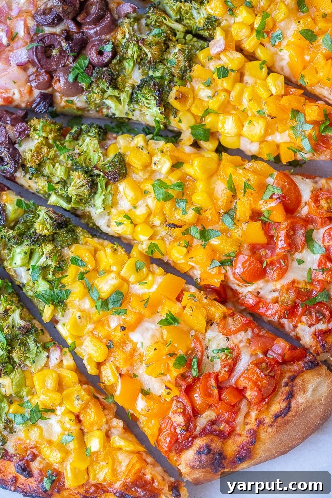 Kaleidoscope Veggie Pizza 6 A close-up shot of a single slice of rainbow vegetable pizza, held up to show the distinct layers of colorful vegetables and melted cheese on a perfectly browned crust. The vibrant colors are appealing and the slice looks ready to eat.