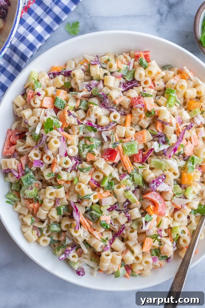large bowl of macaroni coleslaw salad with a serving spoon, garnished with fresh herbs