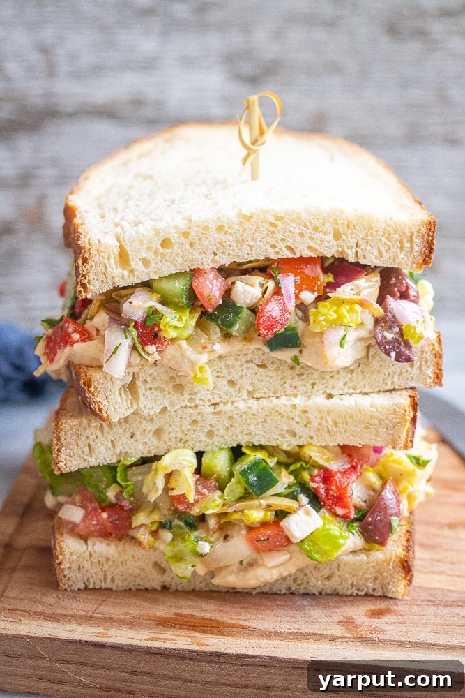 Zesty Greek Hummus Sandwiches 5 A freshly made Greek Salad Sandwich with hummus on a wooden cutting board, ready to be served.