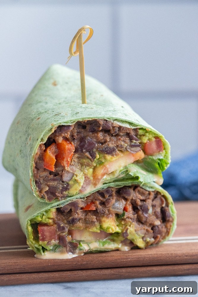 Smoky Chipotle Tahini Black Bean Wraps 5 A perfectly sliced vegan black bean wrap, cut in half and presented on a wooden cutting board, revealing layers of spiced beans, fresh vegetables, and creamy tahini sauce.