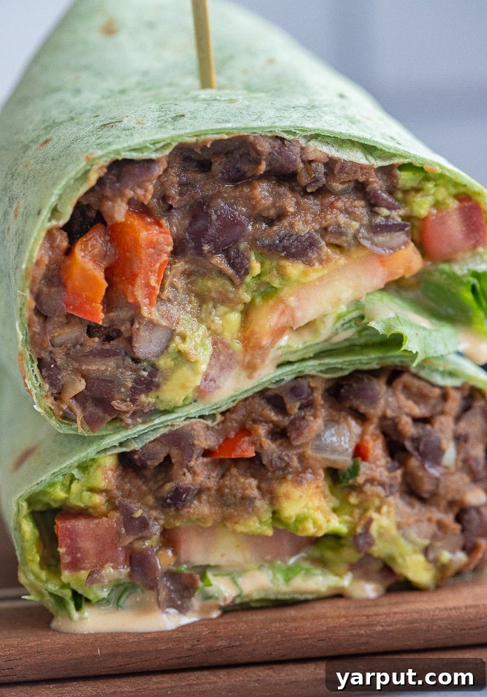 Smoky Chipotle Tahini Black Bean Wraps 6 A vibrant close-up of two stacked vegan black bean wraps, expertly sliced in half and adorned with fresh herbs and a generous drizzle of chipotle tahini sauce, ready to be enjoyed.